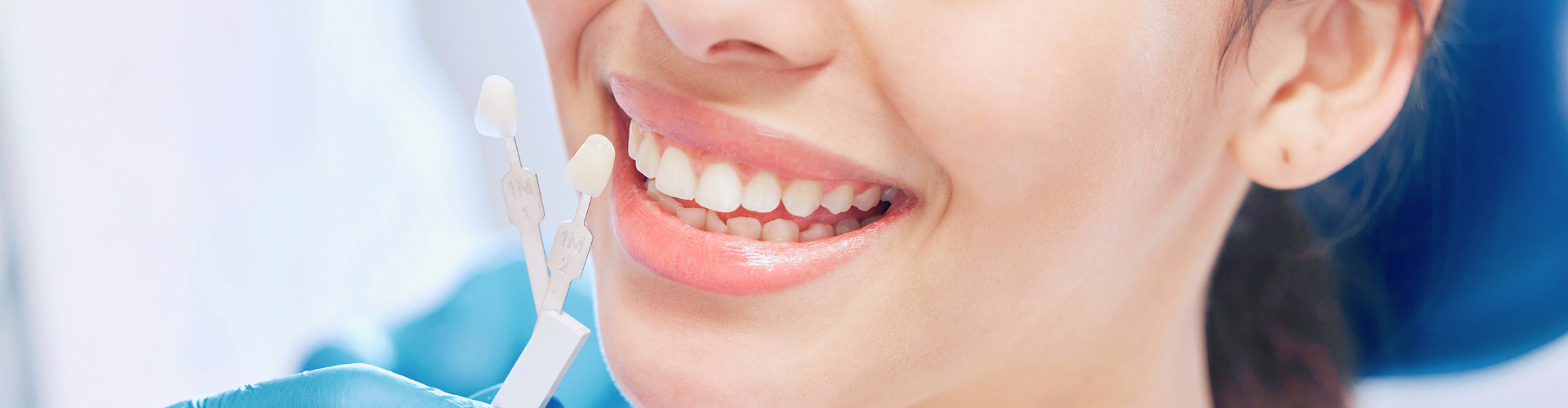 Gloved hand holding tooth shade-matching tool against woman's smile.